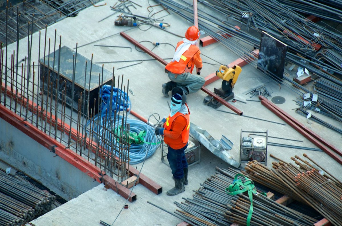 Trabajadores con casco sobre la armadura de acero de una obra